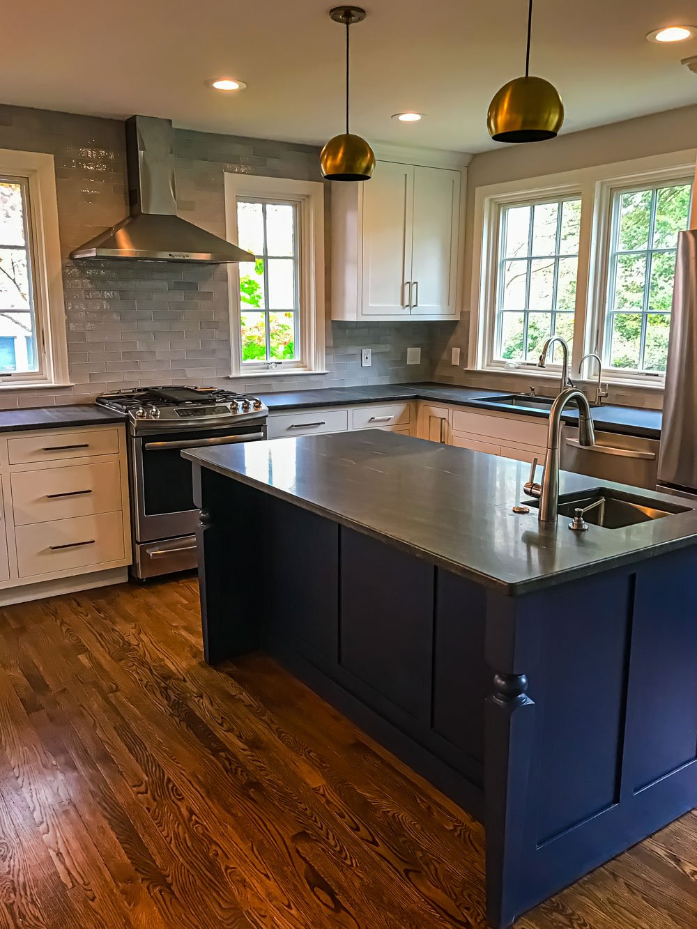 Kitchen renovation featuring stainless steel fixtures, blue wooden island, and many windows for natural light to open the floorplan