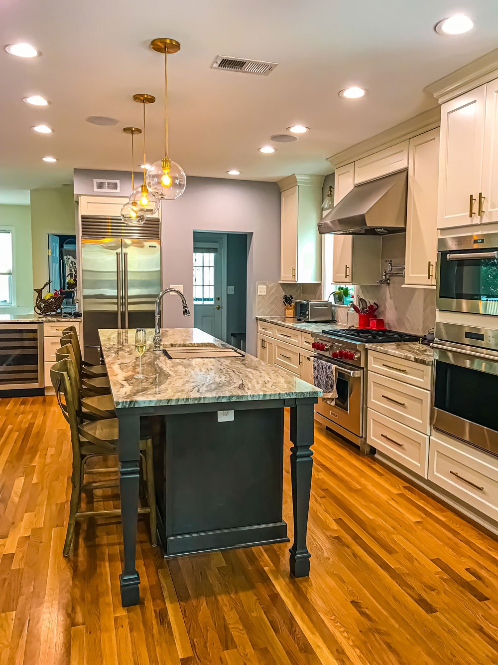 Remodeled kitchen with eight ceiling can lights and gold hanging lights above a kitchen island