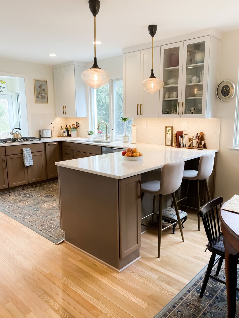 Kitchen island with two bar stools with backrests, a decorative bowl of fruit center piece, and white cabinetry with glass panelling
