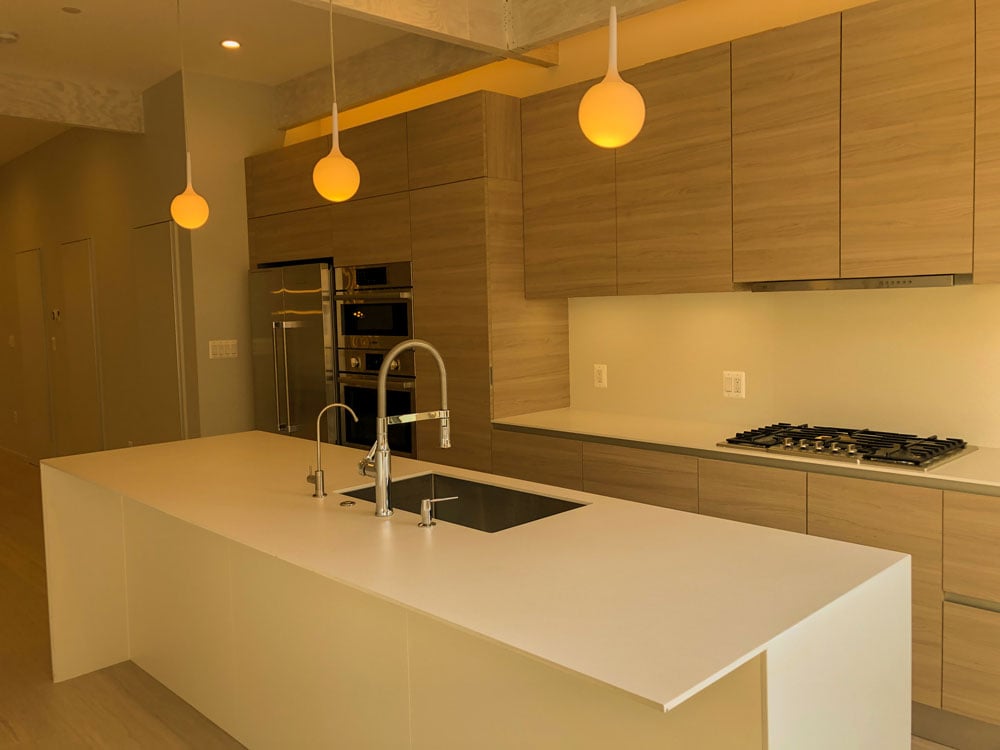 White simplistic kitchen island with hanging lights that give off a warm orange light