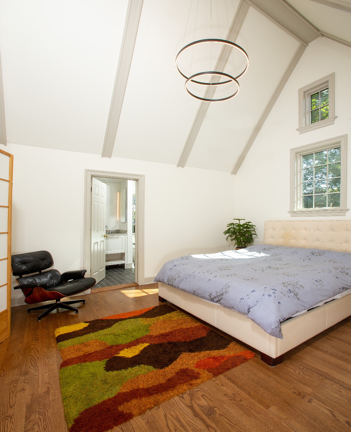 Bedroom with high-loft cathedral ceiling, elegant hanging light fixtures, and colored roof beams