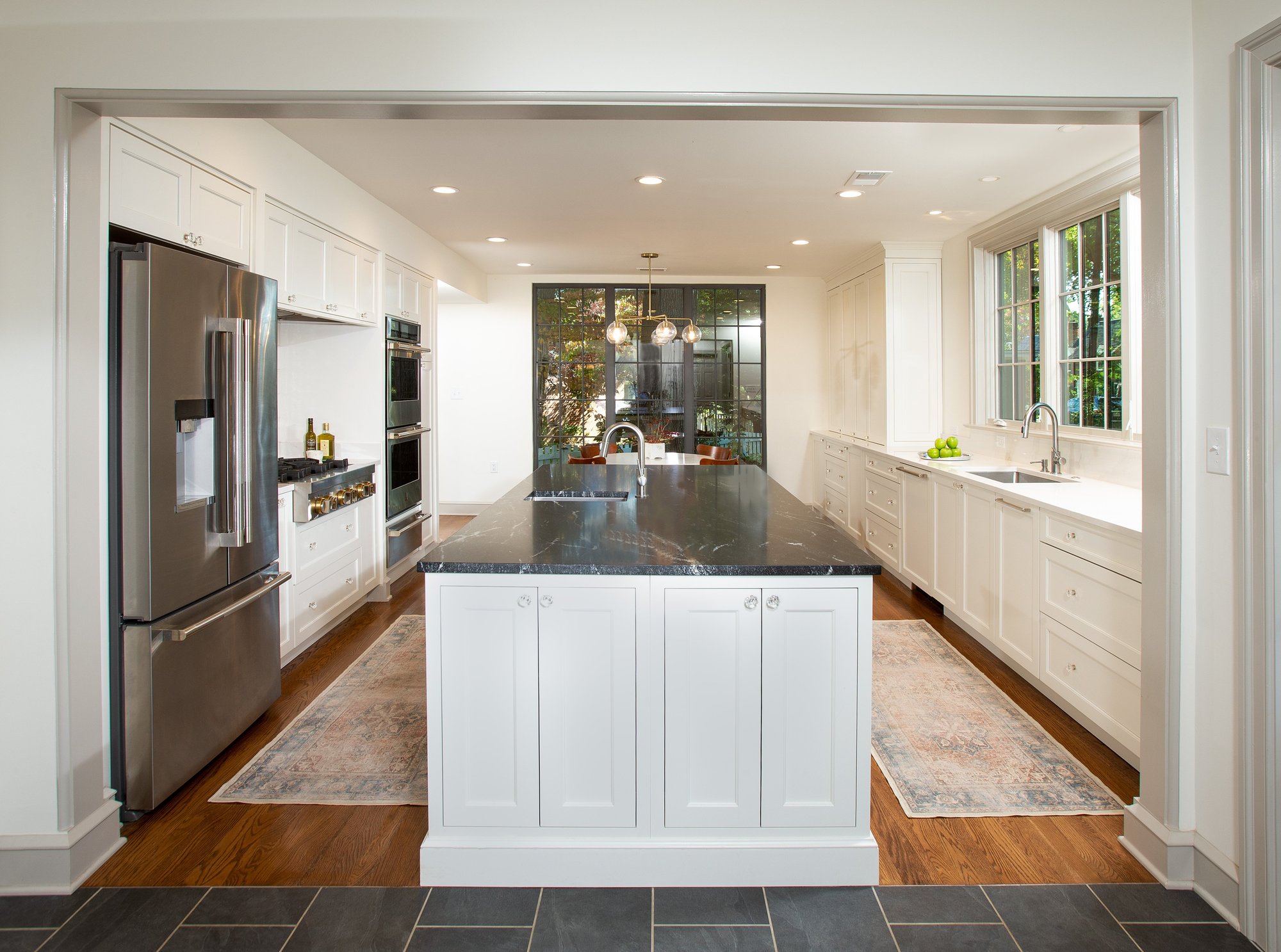 Luxury kitchen remodel with a long kitchen island, black marble countertops, and white storage spaces