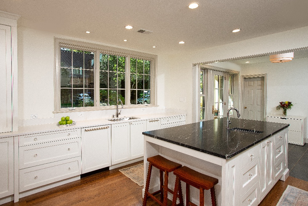 Kitchen with hard white can lighting, bar stool seating at the kitchen island, and natural light over the sink