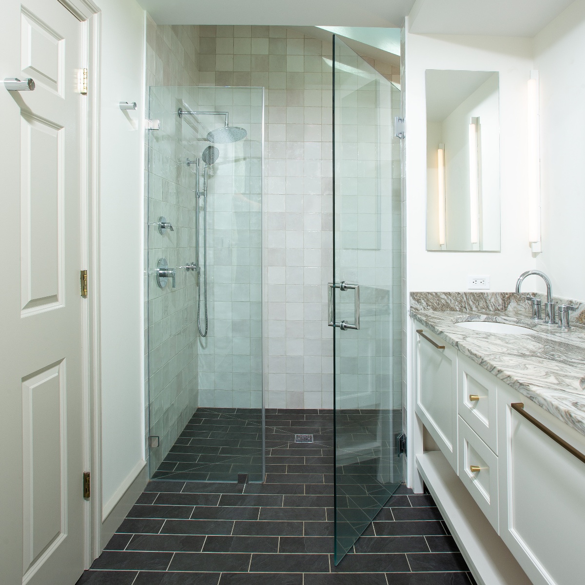 Bathroom with glass walk-in shower, and white wood cabinets and doors, and black tile flooring