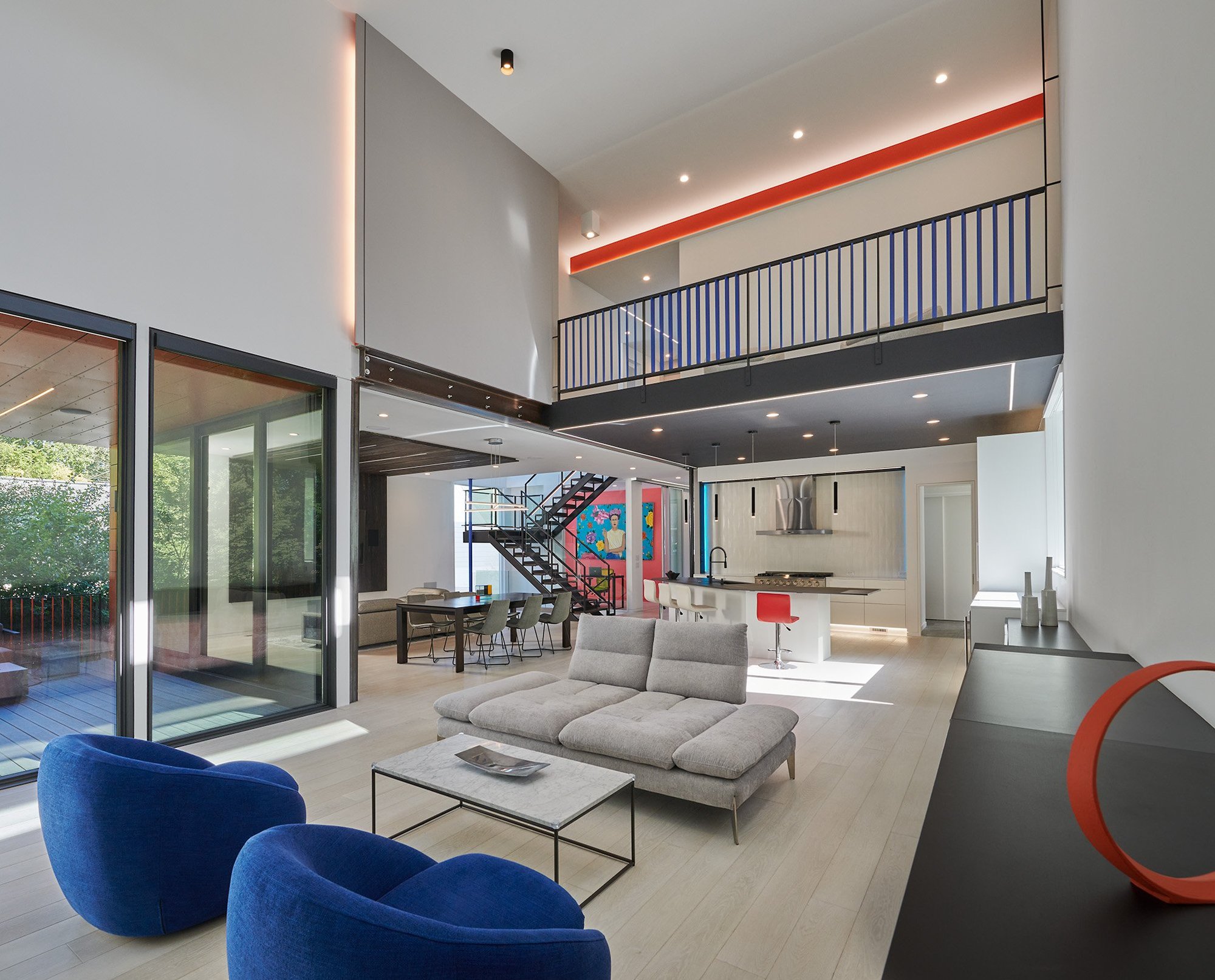 Living room of modern home with a kitchen and staircase in the background.  An open balcony over looks the room.