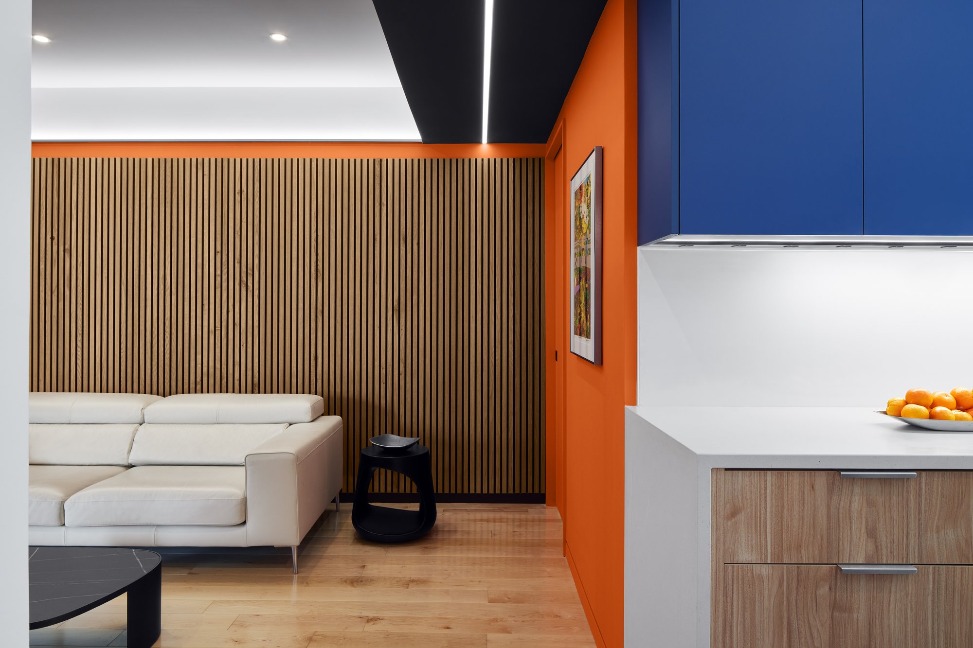 A family room with decorative wood paneling, orange wall, and white sofa.  The transition to the kitchen can be seen to the right. 