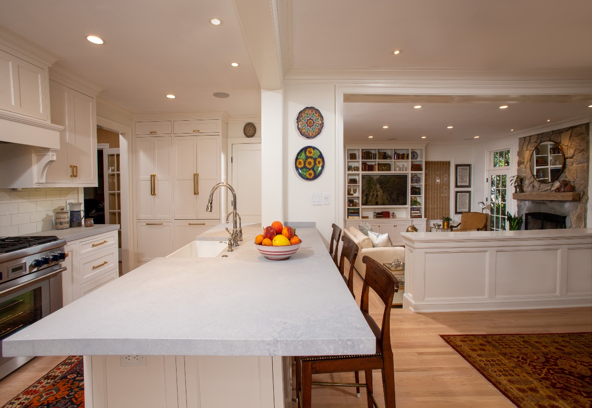 Kitchen countertop in foreground with three wooden seats, and family living room in the background