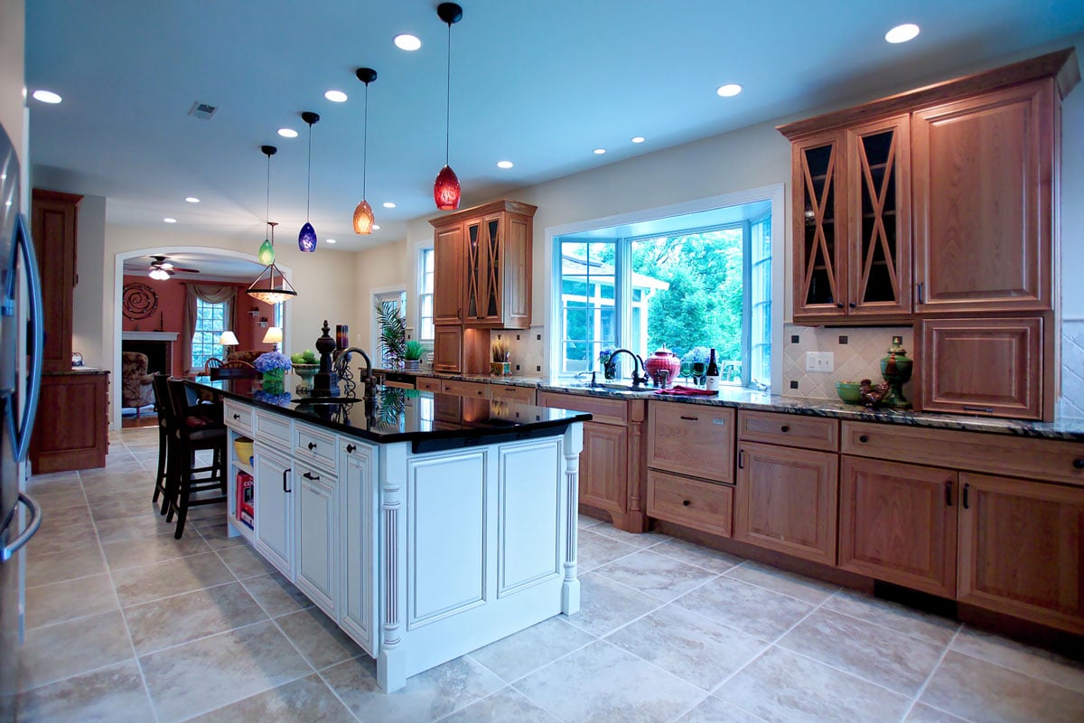 Natural wood kitchen cabinetry with tan tiling and multicolor lamps