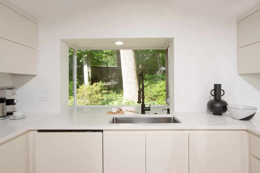 Kitchen sink in front of large window looking outside to a forest