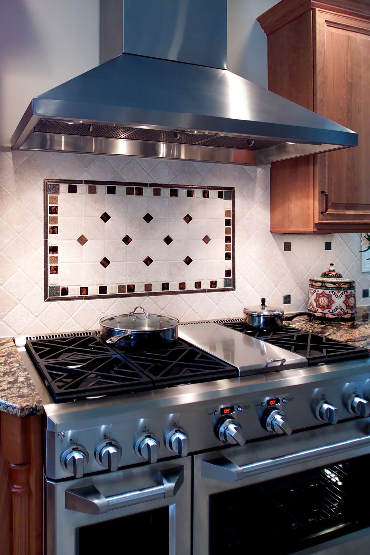 Stainless steel oven with stainless steel exhaust hood and geometric tile backsplash pattern