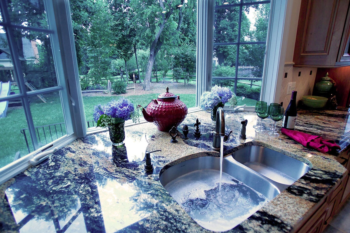 Kitchen sink with running water in front of three-pane window overlooking a garden backyard