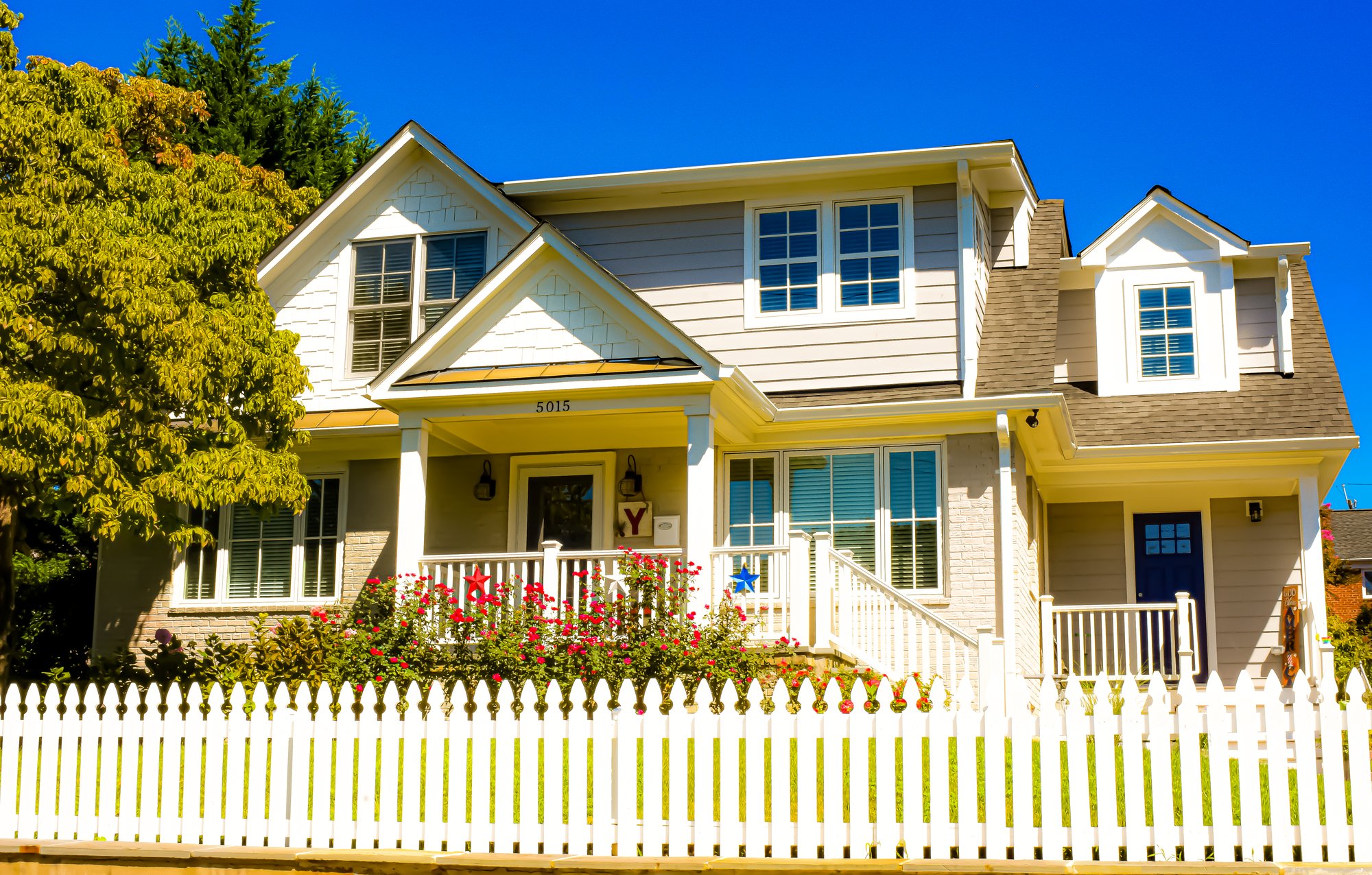 Front of home with a white picket fence and radiantly blue sky.