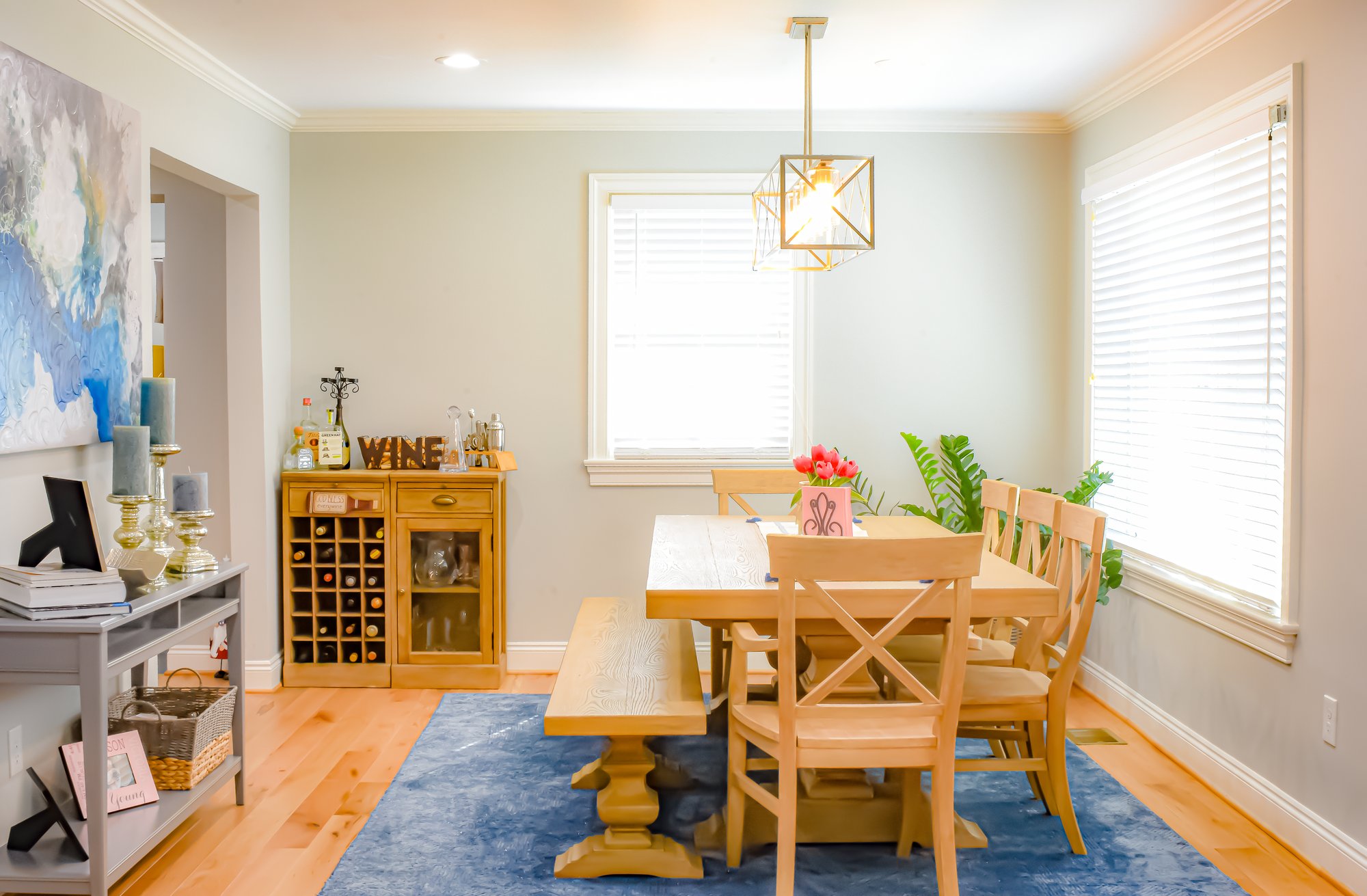 Dining room with wooden dining room table, blue area rug, and wooden and glass bar. 