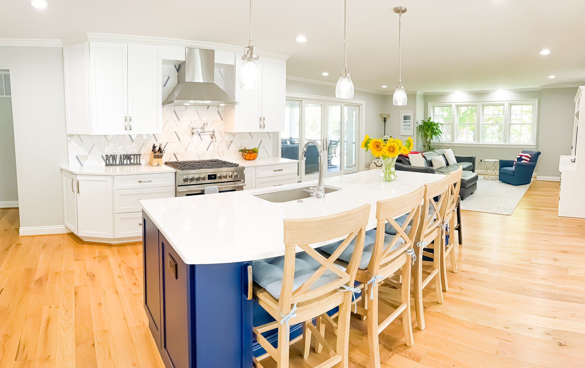 A bright kitchen featuring an island with four bar chairs.  A family room sits in the background.