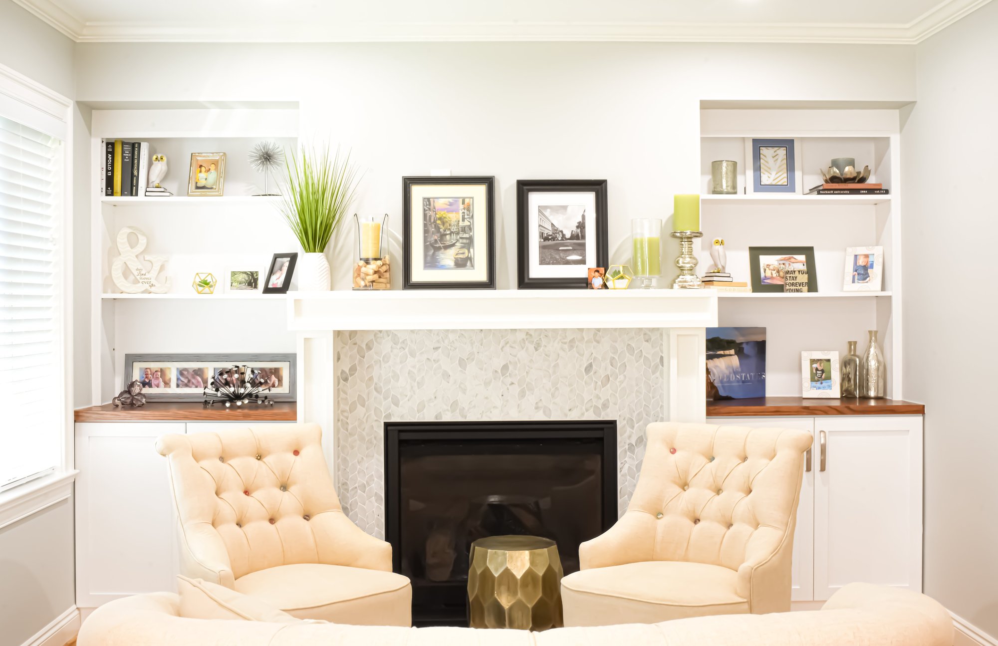 Living room with a fireplace featuring a tiled hearth.  Bookshelves and cabinets frame both sides of the fireplace.  Two cream colored armchairs face away from the fireplace. 
