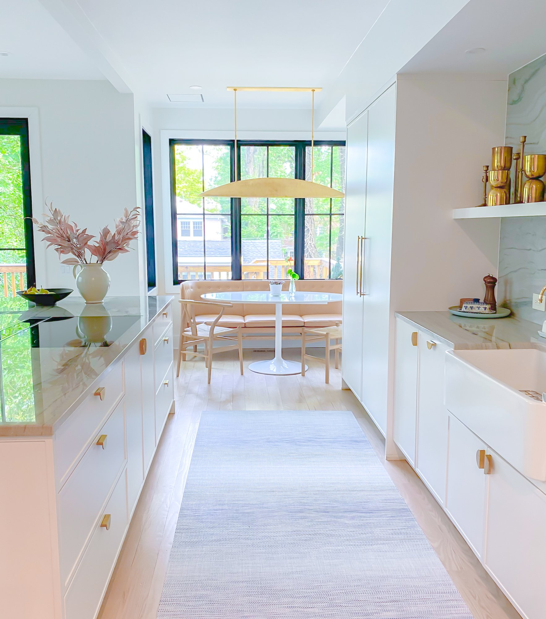 Pure white kitchen walkway with white polished floors, white storage spaces with gold accents, and lots of natural light